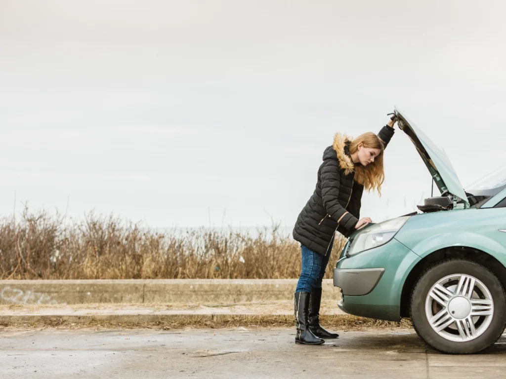 Woman on roadside checking under the hood of her car